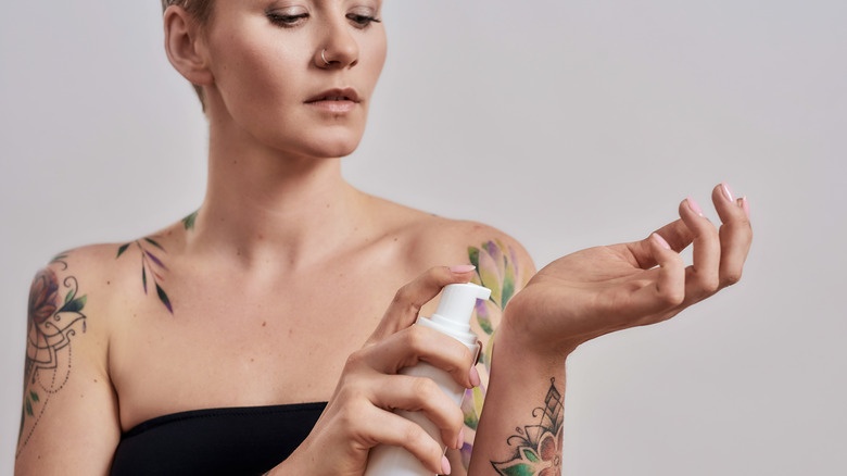 tattooed woman applies lotion