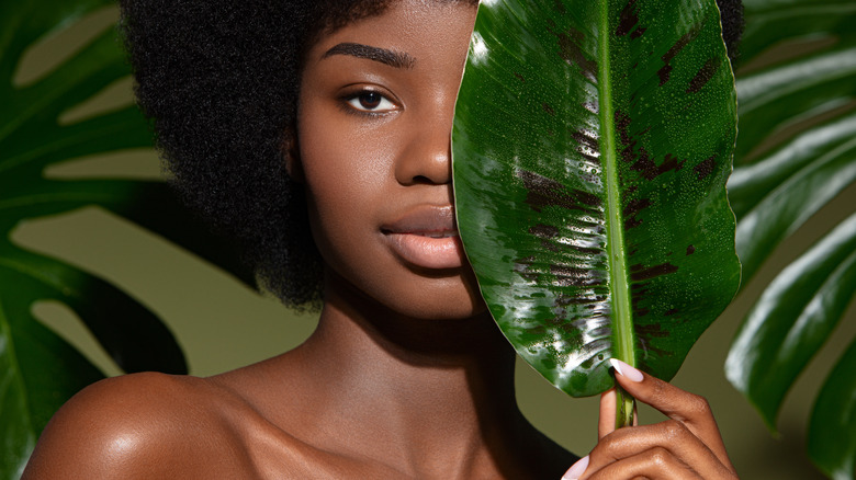 black woman holding leaf with clear skin