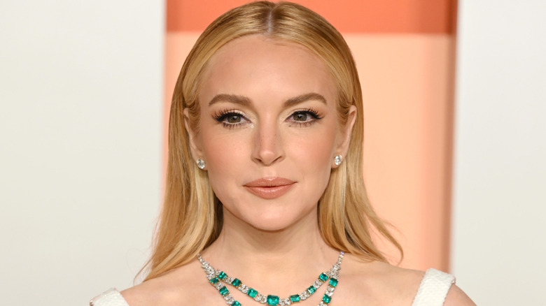 Lindsay Logan smiling while wearing a white dress and an emerald necklace