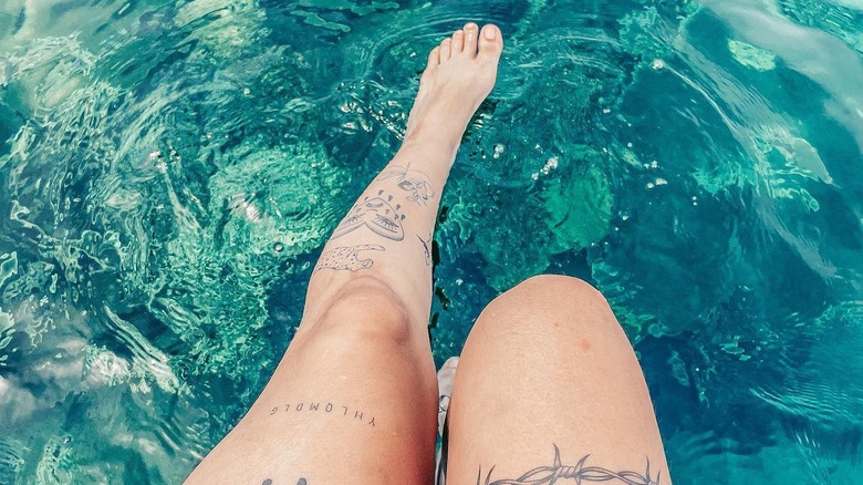 tattooed female legs in swimming pool