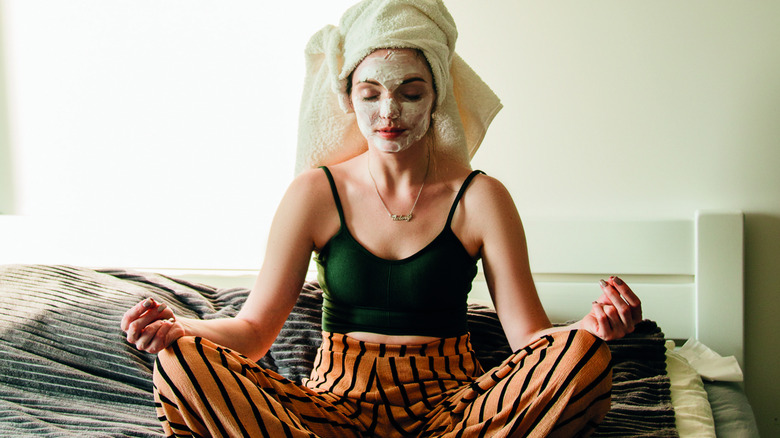A woman meditating with a face mask on and a towel wrapped on her head