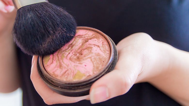 Hand holding bronzer dish with brush dipped in