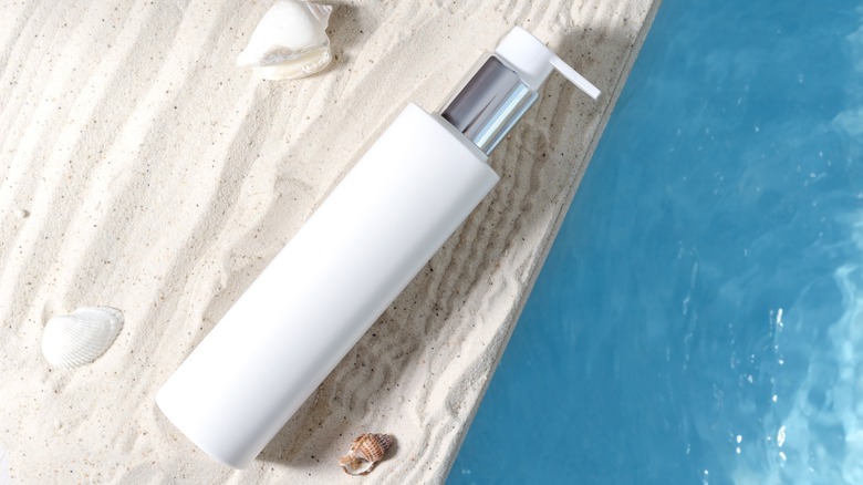 sunscreen bottle in sand next to water