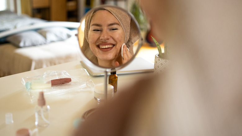 A woman with acne scars looking in a mirror