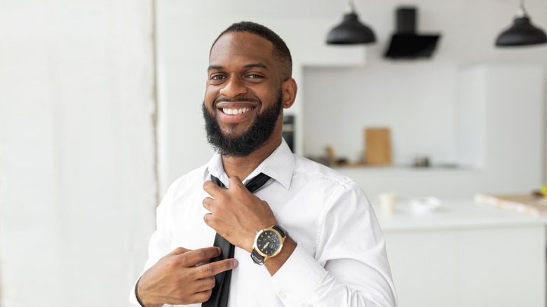 Smiling man putting on tie