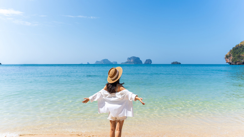 Woman on a beach facing the ocean with arms out