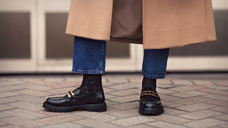 Black loafers and blue jeans and a tan coat