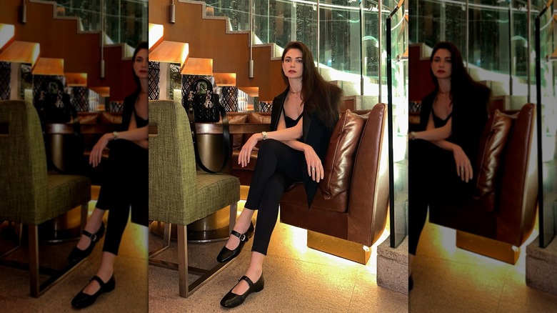 A woman wearing trousers and Mary Jane shoes sitting in a chair