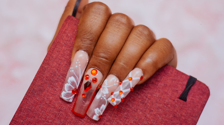 A hand with long square-shaped fake nails with different floral patterns and embellishments