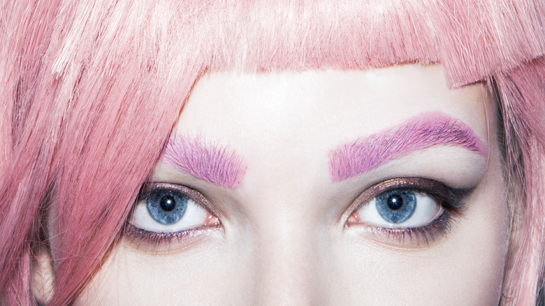 Closeup of a woman's eyes with pink hair and eyebrows.