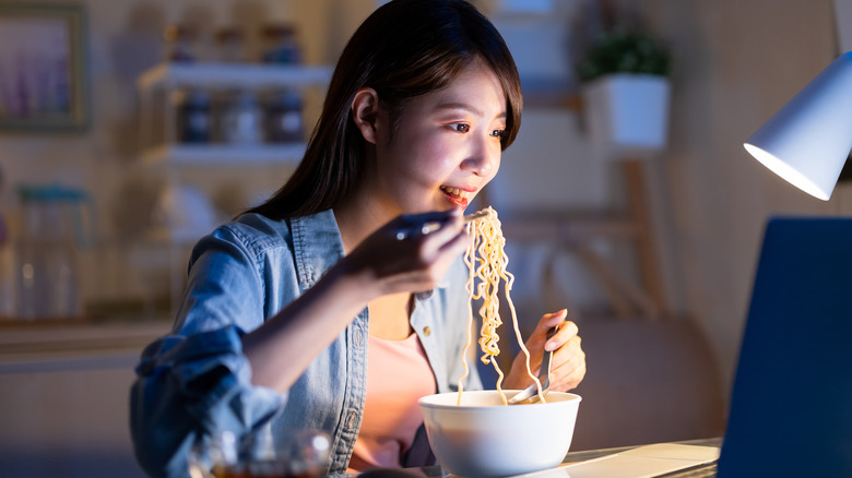 Woman happily eats ramen in front of laptop