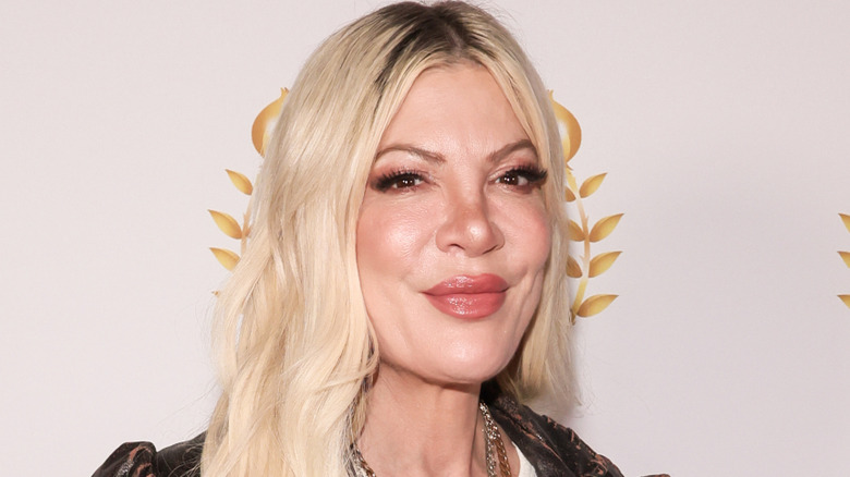 Tori Spelling wearing a white top with layered necklaces