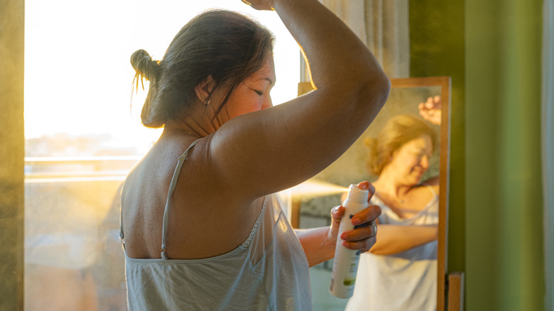 Woman spraying on deodorant in front of mirror