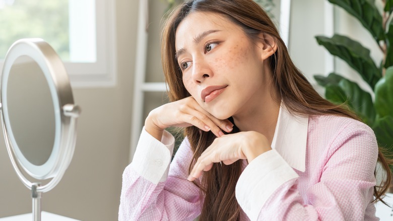 Asian woman with hyperpigmentation looking in mirror
