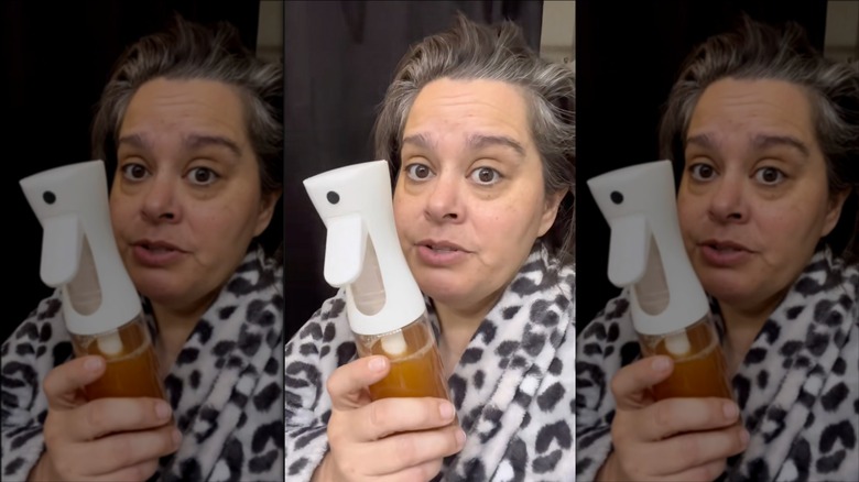 A woman holding a spray bottle filled with apple cider vinegar