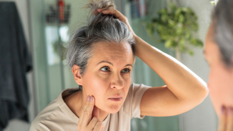 A woman examining her gray hair in a mirror