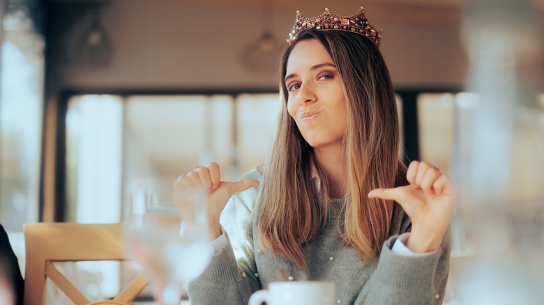 Tiara-wearing woman pointing at self