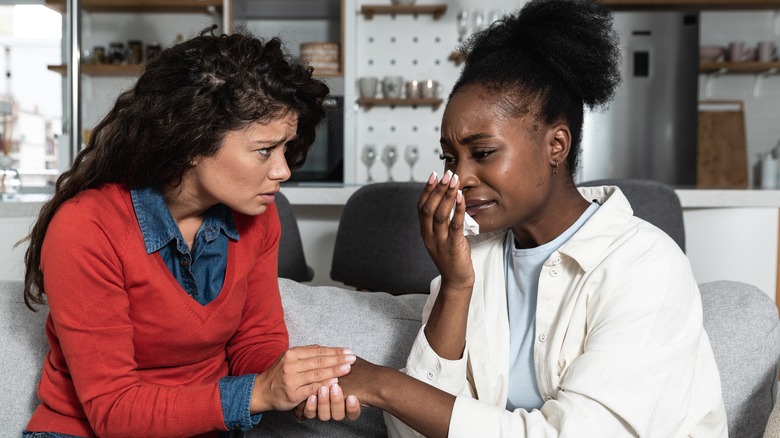 Woman crying with friend holding hand