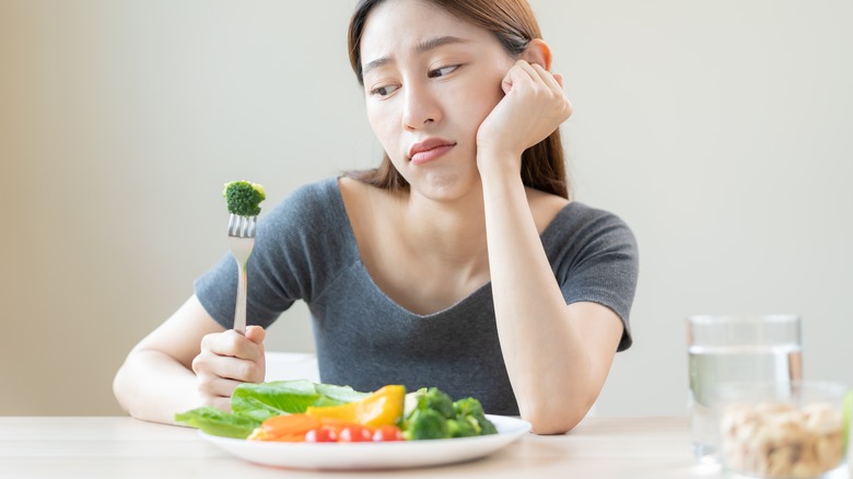 Woman stares at vegetables unhappily