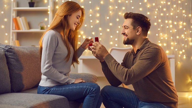 A man proposing to a woman at home in front of fairy lights