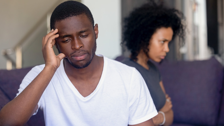 Man looks regretful with upset woman in background