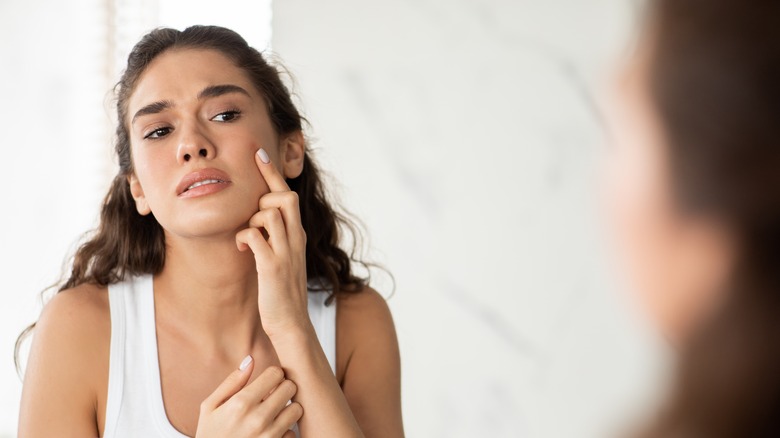 woman looking at acne in mirror