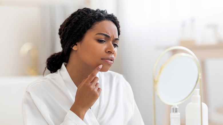 woman looking at skin in mirror