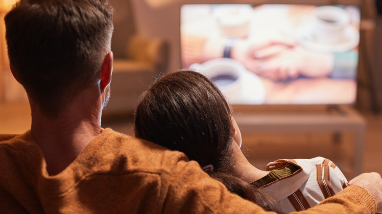 the back of a couple watching tv together in a muted room