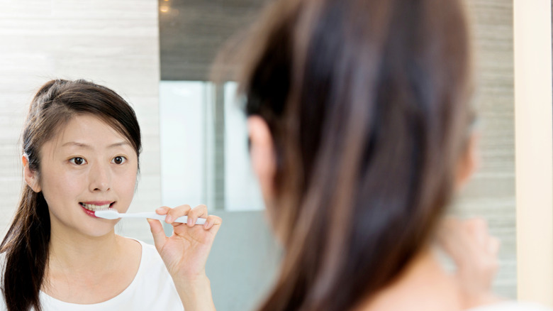 woman brushing teeth in mirror
