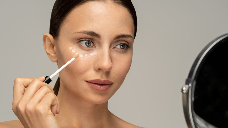 woman applying concealer in mirror