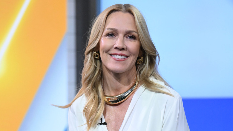 Jennie Garth wearing white button down and gold chunky necklace smiling.