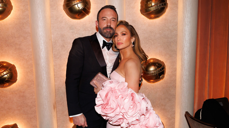 Ben Affleck wearing a suit and Jennifer Lopez wearing a pink ruffled dress posing together at a red carpet event.