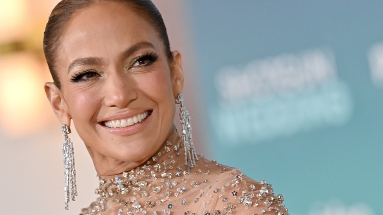 Jennifer Lopez smiling at an event wearing a sparkly outfit and statement earrings.