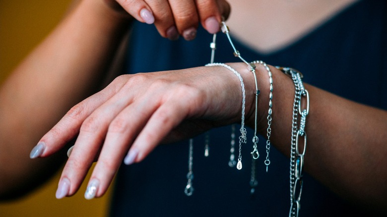 A woman draping silvery jewelry over her wrist.