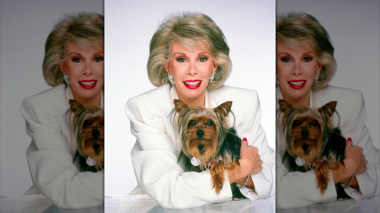 Joan Rivers smiles in a white suit while holding a dog.