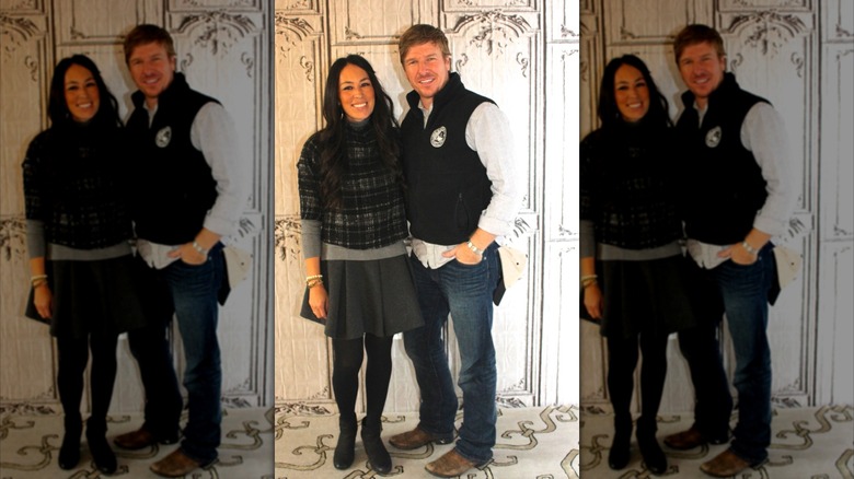 Joanna Gaines and Chip Gaines posing together against an ornate white wall.