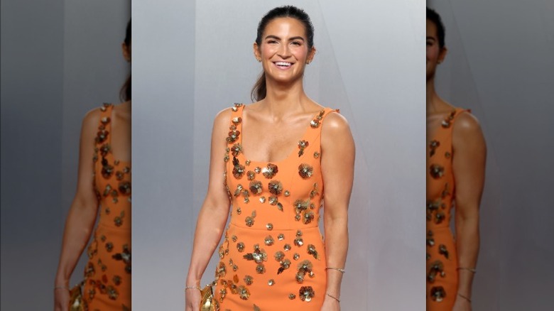 Kaitlan Collins smiles while wearing an orange gown with gold embellishments.