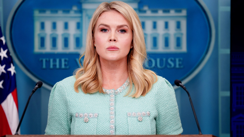 Karoline Leavitt wearing an aging teal outfit with a displeased look on her face