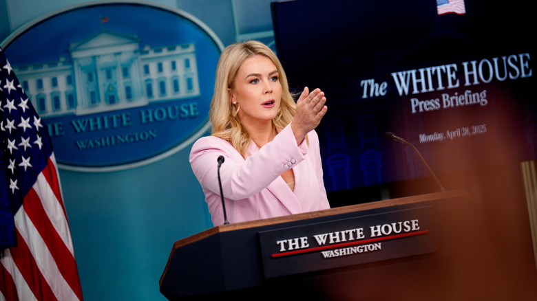Karoline Leavitt speaking at a podium in a pink blazer