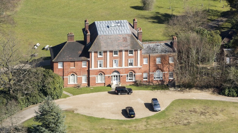 An image of Forest Lodge, Kate Middleton and Prince William's new home. It is a large brick home with many windows, surrounded by lush green.