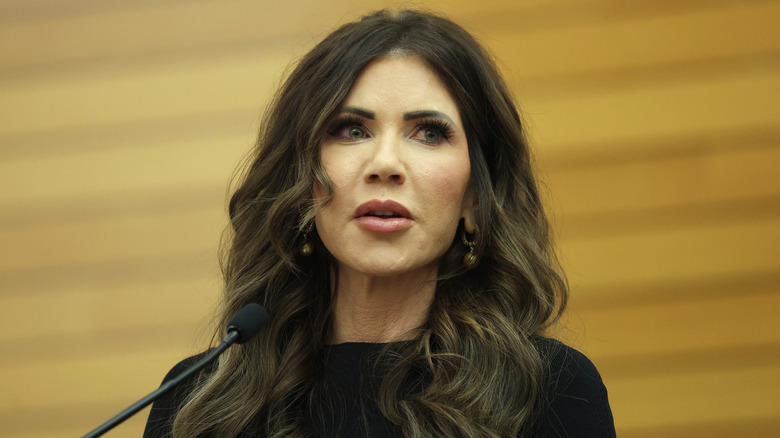 Kristi Noem wearing a black outfit and luxury jewelry delivers remarks at the Assumption of Command Ceremony