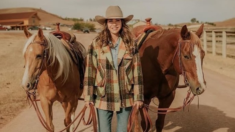 Kristi Noem posing in a plaid jacket and cowboy hat leading two horses