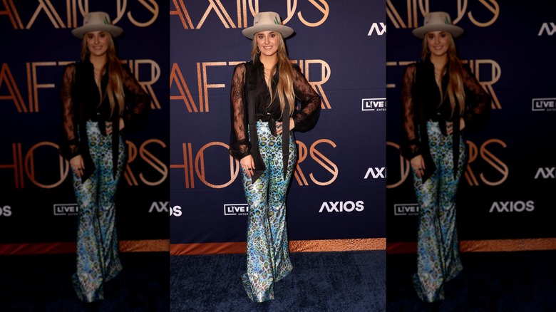 Lainey Wilson wearing blue leopard-print pants with a black lacey top and a cowboy hat