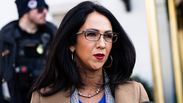 Closeup of Lauren Boebert wearing glasses while speaking to the press outdoors.