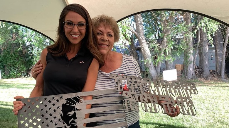 Lauren Boebert holding Trump merchandise while wearing black sleeveless polo top and glasses