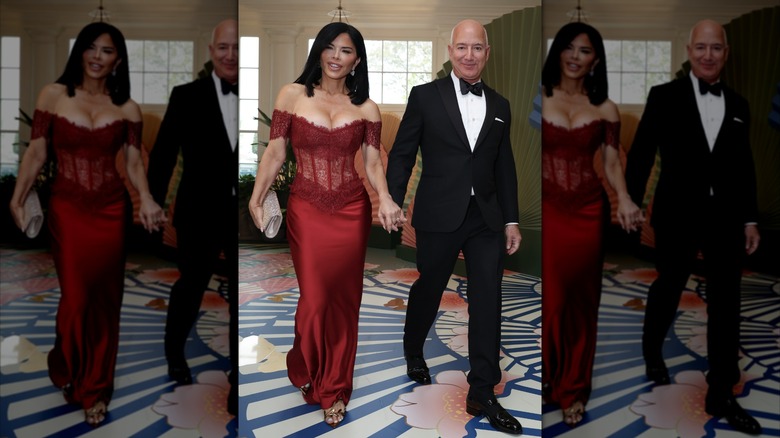 Lauren Sánchez Bezos and Jeff Bezos enter an event at the White House. Sanchez is wearing a form-fitting gown with a lace bodice and low neckline. Jeff is wearing a black tuxedo with a white shirt underneath.