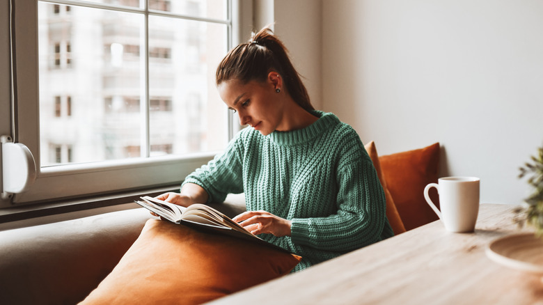Woman reading book beside window