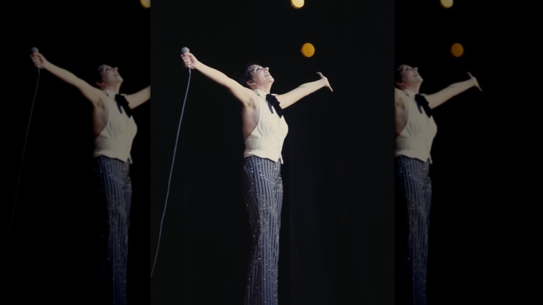 Liza Minnelli performing on stage with a microphone in her hand with her hands in the air.