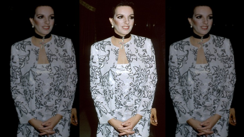 Liza Minnelli posing with her hands clasped wearing a white and black outfit and a black choker necklace.