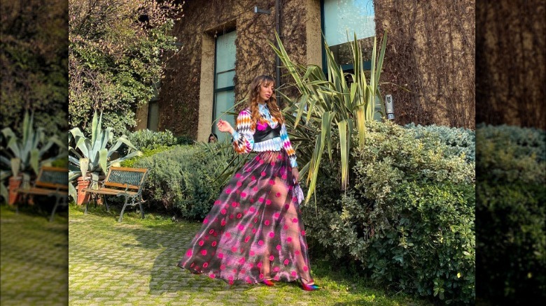 Woman wearing patterned sweater, shirt, and skirt